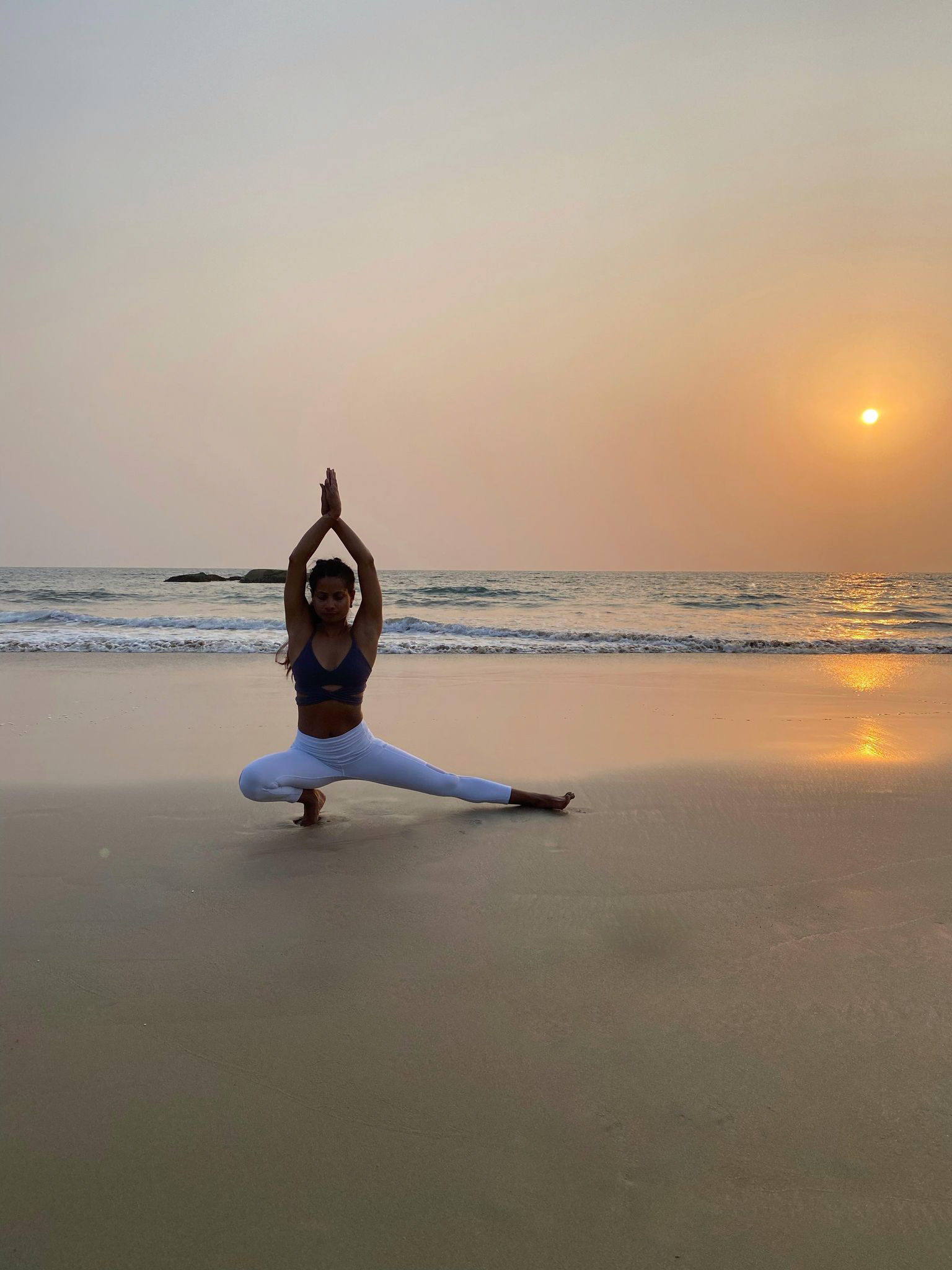 woman doing yoga on beach at sunset